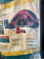 Packaging showing a four-person dome tent in red and blue with two folding chairs, two 1.5 lb sleeping bags, and a 12-can cooler included in the set.