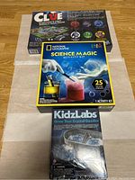 Photo showing sealed boxes of Clue board game, National Geographic Science Magic kit, and KidzLabs Grow Your Crystal Geodes kit.