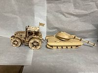 Wooden mechanical tractor and tank models placed side by side against a paper background.