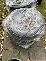 Four winter tires on rims wrapped in plastic from a top perspective, showing tread condition and packaging.