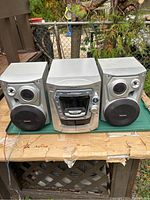 Front view of Panasonic music centre with two detached speakers on wooden table outdoors.