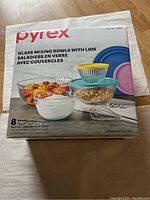 Front of the sealed Pyrex box showing 4 glass mixing bowls and 4 lids in different colors (yellow, blue, pink, turquoise), and images depicting the bowls with ingredients.