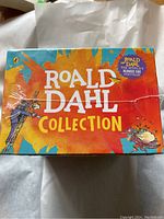 Top side view of the orange and blue Roald Dahl Collection box showing the name with colorful splashes and illustrations.
