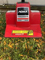 Close up front view of the red labeled NOMA Turbo Shovel 1200 unit on grass showing brand and model.