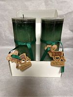 Two green pillar candles with ribbons and wooden reindeer tags displayed in white holder