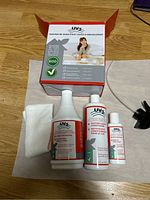 Set of three UV3 upholstery care product bottles, white cloth, and original box on wooden floor