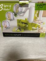 Front of the box showing the slicer with three types of blades: curl, slice, and julienne. Branding KitchenStuff, Veggi Twist Spiral Slicer, 4 piece set.