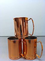 Set of three copper mugs stacked, showing their shiny copper plating and handles