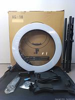 Boxed 18 inch LED ring light with the packed tripod stand and accessories arranged in front, showing the ring light ring and tripod legs.