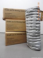 Three boxed body heating pads stacked with one heating pad folded showing their boxes and packaging text.