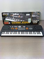 Front view of BIGFUN 61 key electronic keyboard with box behind showing product image and branding.