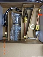 Photo showing boxed faucet components including curved spout, two handles, and parts for installation in chrome finish.