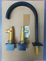 Top view showing matte black faucet spout and two valve assemblies marked with red and blue for hot and cold water control. The faucet connects via a widespread 3 hole deck mount.