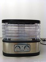 Front view showing the full food dehydrator unit with five clear stackable trays and stainless steel base with two knobs.