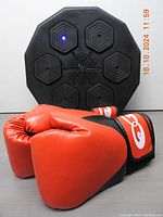 Front view of the black octagonal boxing target with LED light active and the red boxing gloves in front.