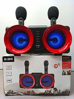Photo of karaoke speaker and packaging box displaying model AL-307S with blue lighting speakers surrounded by red rings and two microphones.
