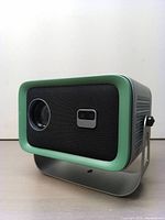 Front and side angle view showing projector lens and speaker grill with green trim and mounting stand.