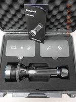 Open black plastic case with foam insert containing flashlight and user manual