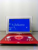 Red Jekero portable DVD player open with screen on showing 'Jekero' text, key buttons and disc tray area visible.