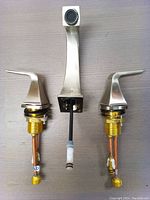 Silver two handle widespread bathroom faucet with separate hot and cold handles and center spout, showing copper plumbing connections and mounting hardware underneath handles.