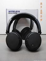 Front view of black wireless headphones showing ear cups and headband with the product box in the background labeled 'Wireless Headphone'