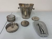 Full view of the entire champagne serving lot itemized on table surface showing ice bucket, coaster holder, coasters, and champagne pliers with case.