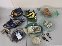Top-down image showing all fish-shaped ceramic bowls, glass trays, wooden utensils, and assorted fish-themed drink stoppers and accessories arranged on table.