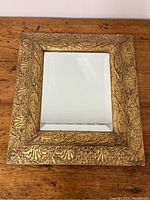 Top-down photo showing entire rectangular gilt frame mirror with carved shell and leaf motifs on frame and beveled glass.