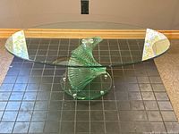 Top view of oval tempered glass tabletop with visible slight wear on edge and scratches on surface.