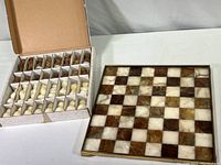 Photo showing open box with agate chess pieces arranged in compartments adjacent to the agate-tiled chessboard resting on table.