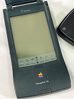 Close-up of Apple Newton MessagePad 130 device showing screen and front panel with multiple buttons and Apple rainbow logo.