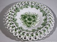 Front of white ceramic decorative plate with hand-painted green floral patterns and perforated scalloped rim