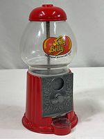 Full view of the Jelly Belly candy dispenser showing the glass globe, red metal base and lid, coin slot and crank on front with embossed metal plate.