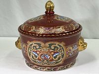 Front side view of large maroon decorative pot showing hand-painted gold accents and lion head handles.