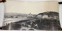 Panoramic black and white photo showing coastal landscape with original Cliff House on cliff, beach and dunes in foreground.