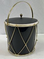 Black insulated ice bucket with lid set inside a gold metal wire holder with a carrying handle, showing full bucket and design details.