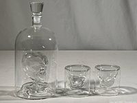 Full set photo showing the decanter with glass stopper and two matching skull design glasses