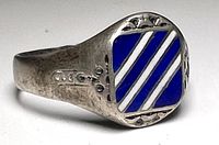 Front view showing the square top of the ring with blue enamel and white diagonal stripes plus decorative silver designs on top edges.
