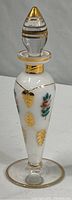 Full view of the vintage perfume bottle showing overall shape, white glass body with hand-painted flowers and gold accents, and stopper with gold bands