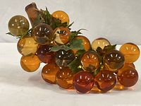 Full view of vintage decorative grape cluster with amber and orange acrylic grapes on natural wood stem and green plastic leaves.