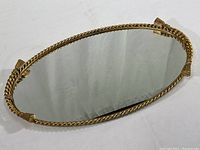 Full view of oval mirrored tray showing gold plated twisted rope frame with tassel accents and mirrored surface.