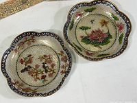 Both plique a jour cloisonné dishes next to each other showing scalloped edges and colorful floral bird and lotus patterns.