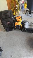 Three bags shown together on floor including black Dakine bag, yellow and black Outdoor Works Alaska 44 backpack and small silver Heys suitcase.