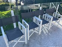 Four folding patio chairs in a row on a outdoor carpet next to glass railing and greenery.