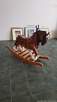 Handmade hardwood rocking horse angled view showing detailed leather harness, fluffy white hoof padding, and wooden rocker base.
