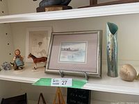 Shelf with framed Picasso archival print, Hummel girl figurine, brown horse figurine, ceramic vase, and stone elephant.