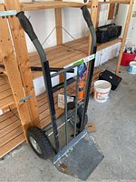 Industrial hand cart showing angled view with black handles and rubber grips, metal frame, and foot plate with surface wear