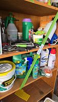 Wide view of shelf with hand tools, various garden tool handles, and several spray containers of weed killers and herbicides