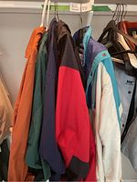 Six different men's jackets hanging on hangers, showing various colors and styles typical of casual outerwear.