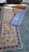 Photo showing floral carpet runner with pastel floral design and other mats, with beige half moon and brown rectangular mat visible